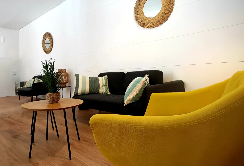 Sala moderna con sillón amarillo, sofás negros, almohadas a rayas, mesa de madera y espejos redondos.