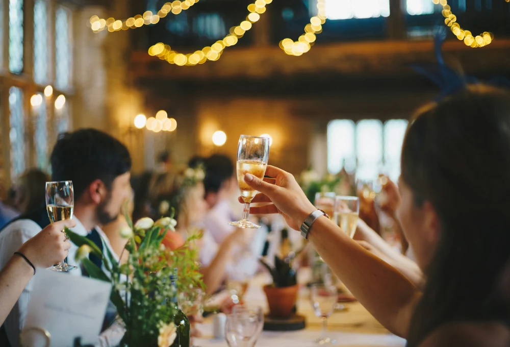 Personas brindando en una celebración con luces y decoración cálida en el fondo.