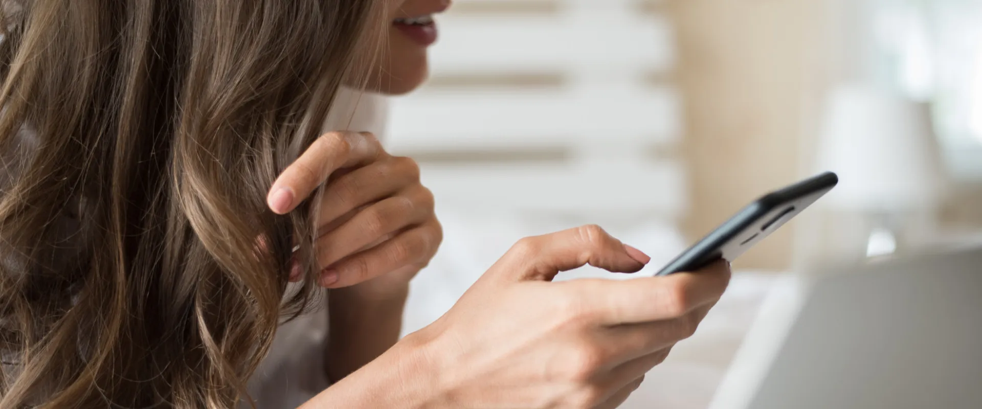 Mujer de perfil sosteniendo un teléfono móvil en una mano, con el fondo desenfocado.