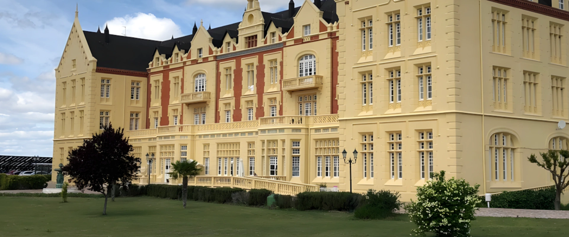 Edificio cl&aacute;sico de varios pisos con fachada amarilla y detalles en rojo, rodeado de c&eacute;sped.