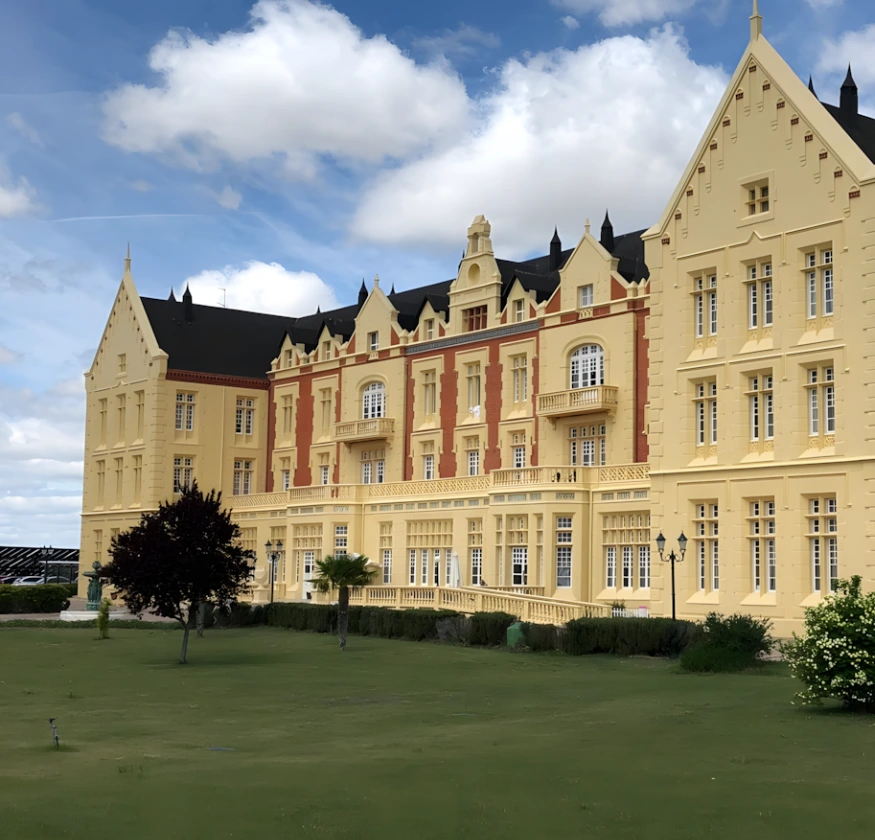 Edificio cl&aacute;sico amarillo con techo negro bajo un cielo azul y nubes.