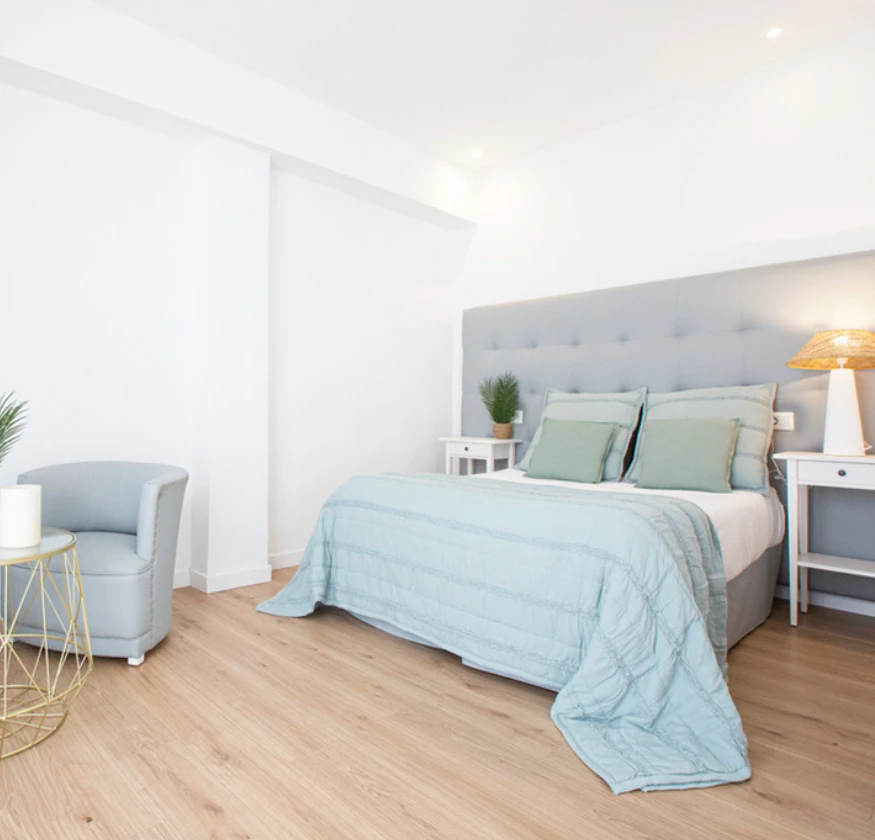 Dormitorio moderno con cama de cojines azul pastel y lámpara en mesita auxiliar.