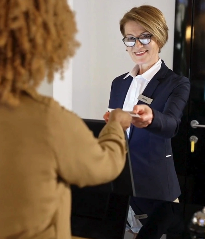 Persona en recepción entregando tarjeta a otra persona, ambas sonríen.