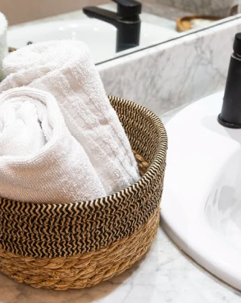 Cesta de mimbre con toallas blancas junto a un lavabo en un baño.