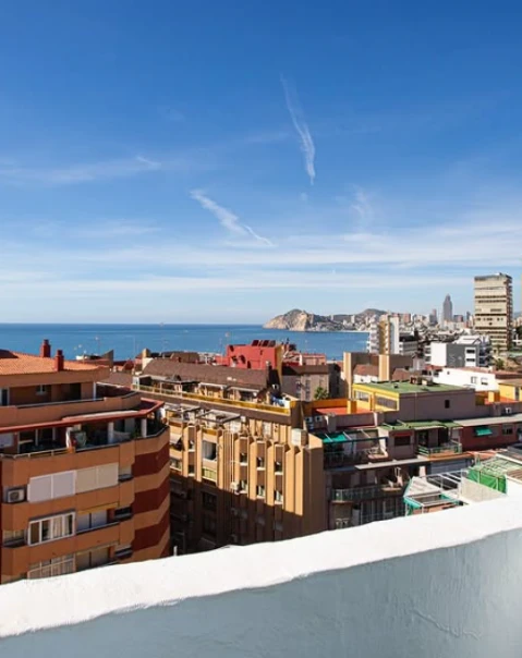 Vista de la ciudad costera con edificios, mar y cielo despejado al fondo.