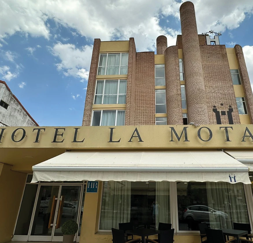 Edificio del Hotel La Mota con fachada amarilla y detalles de ladrillo; cielo despejado.