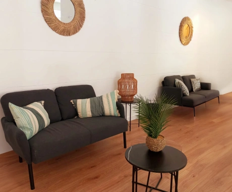 Sala moderna con sofás grises, mesa con planta, espejos y decoración de madera.