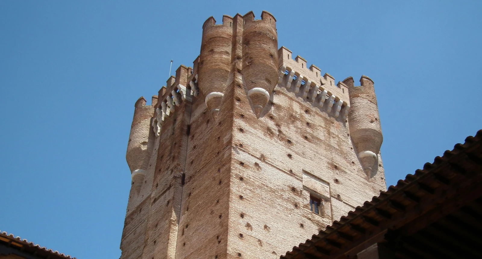 Torre de ladrillo medieval con almenas y cielo azul de fondo.