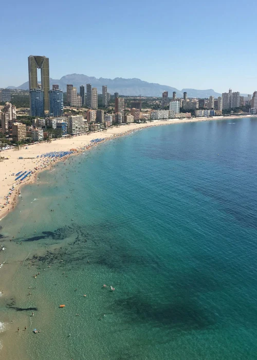 Vista aérea de una playa con edificios altos y montañas al fondo.