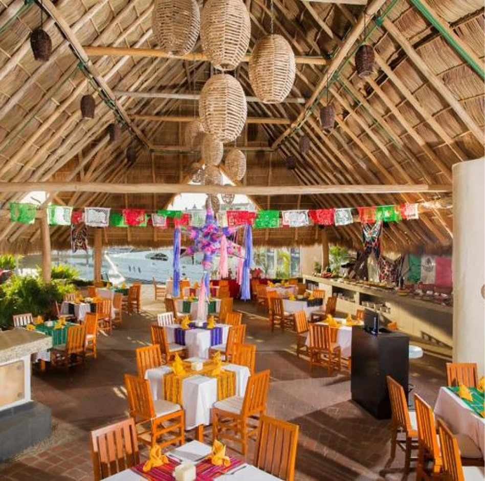 Restaurante decorado con temática mexicana, con mesas de madera y banderines coloridos bajo un techo de paja.