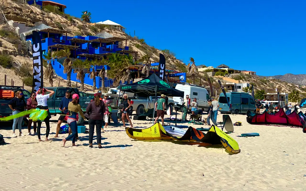 Personas con equipo de kitesurf reunidas en una playa bajo un cielo despejado.