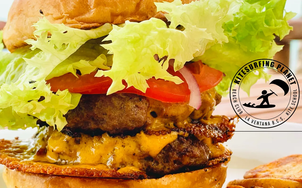 Hamburguesa doble con lechuga y tomate en primer plano, logo de Kitesurfing Planet.