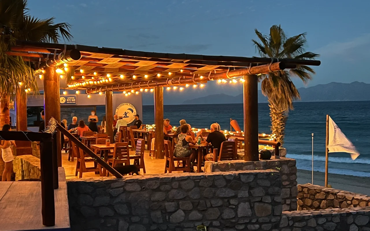 Terraza iluminada junto al mar, gente disfrutando del anochecer.