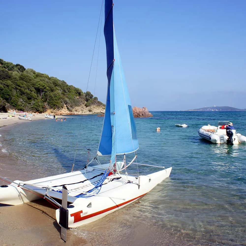 Catamar&aacute;n y lancha en una playa de aguas claras y bosque cercano.