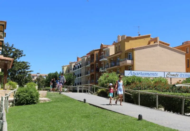 Personas caminando por sendero junto a edificios de apartamentos y c&eacute;sped verde.