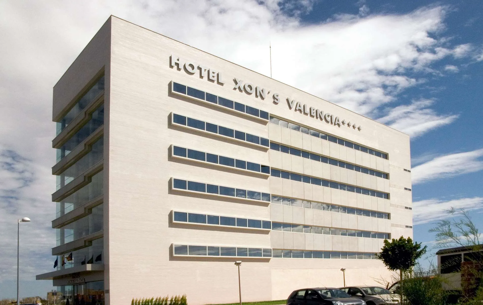 Edificio moderno del Hotel Xon's Valencia bajo un cielo parcialmente nublado.