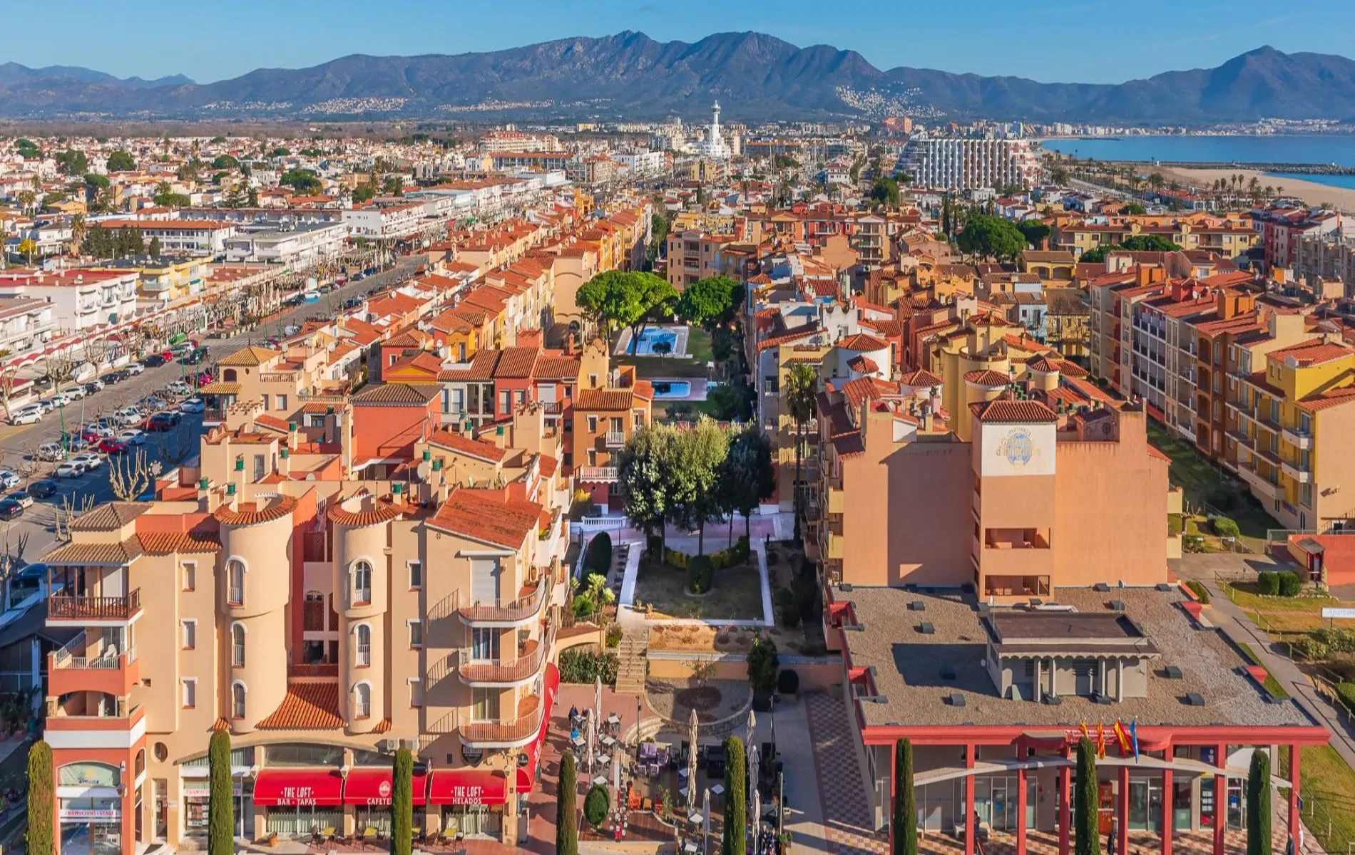 Vista a&eacute;rea de un pueblo con edificios de techos rojos y monta&ntilde;as al fondo.