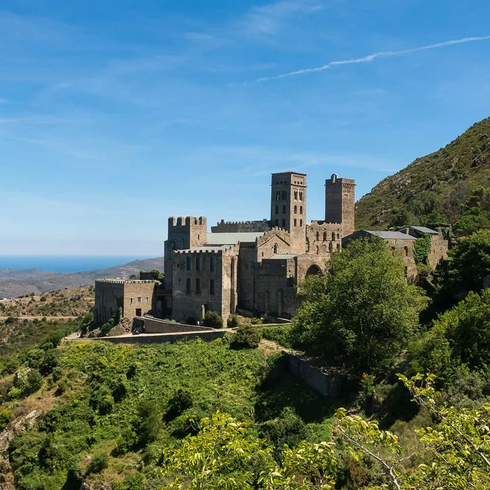 Antiguo monasterio de piedra en una colina rodeado de vegetaci&oacute;n, cielo azul.