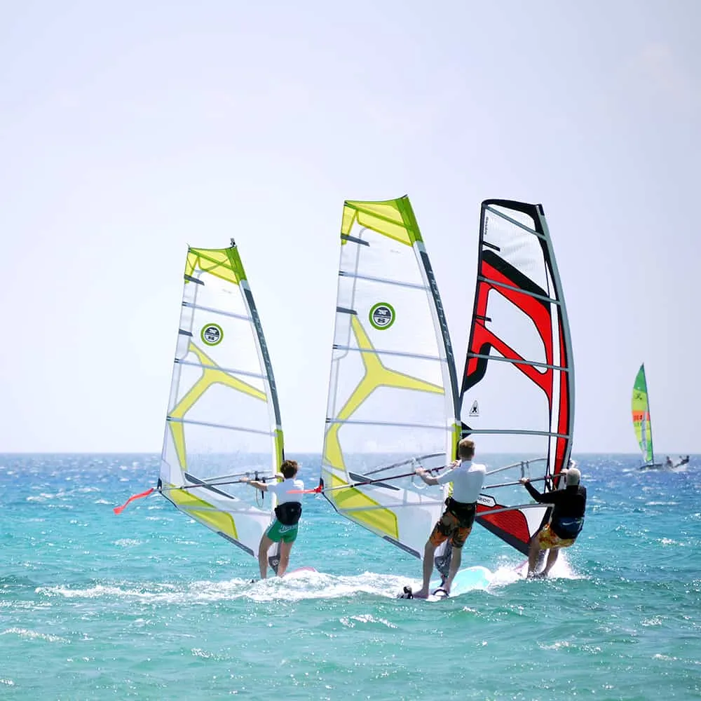 Tres personas practicando windsurf en el mar con velas de colores.