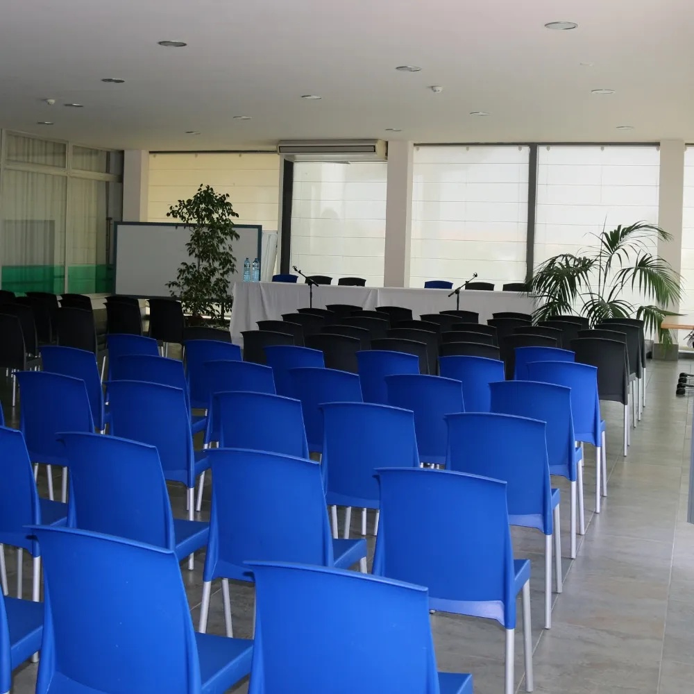 Sala de conferencias vac&iacute;a con sillas azules y negras, frente a una mesa blanca.