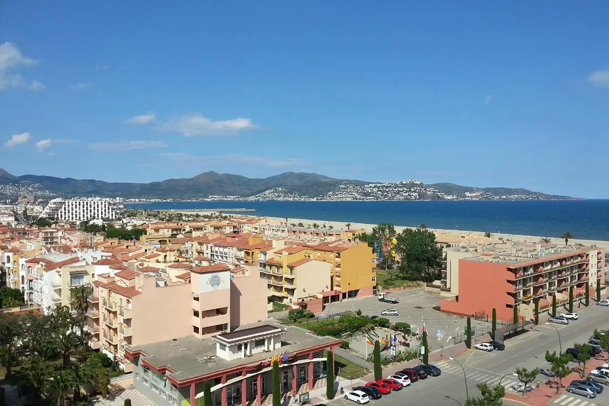 Vista de una ciudad costera con edificios, playa y monta&ntilde;as al fondo.