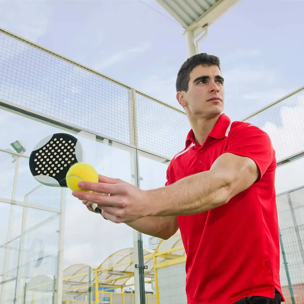 Hombre en camiseta roja sosteniendo una paleta y pelota de p&aacute;del.