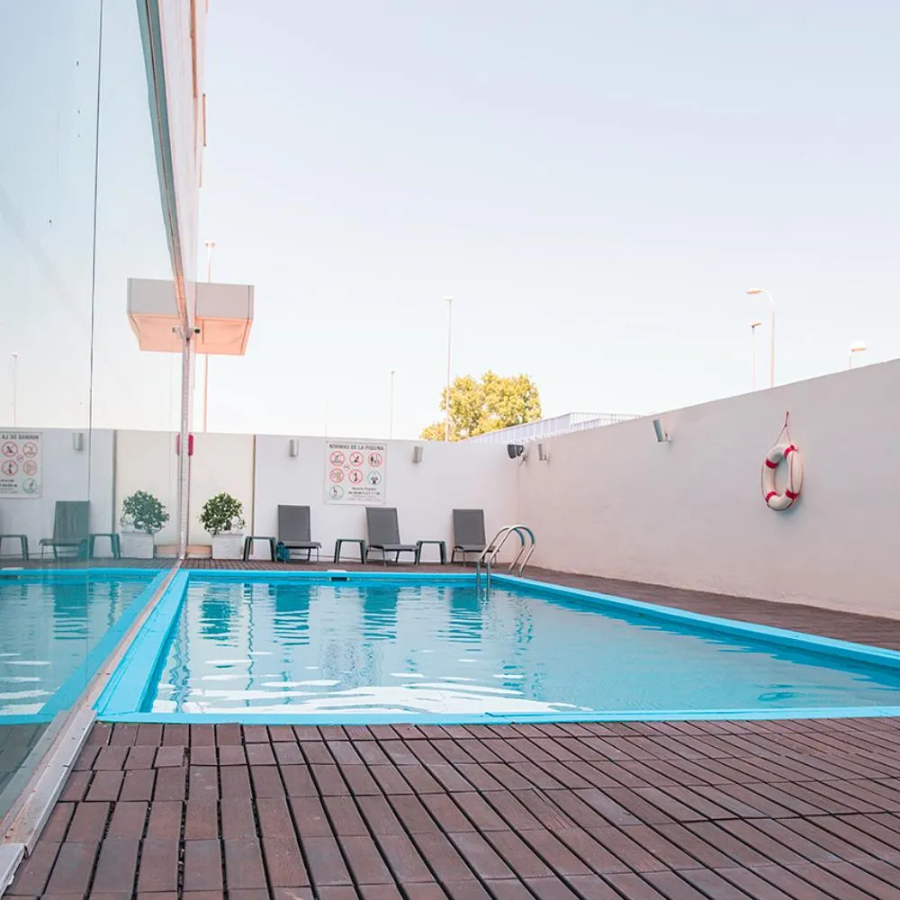 Piscina al aire libre con tumbonas y un aro salvavidas en la pared blanca.