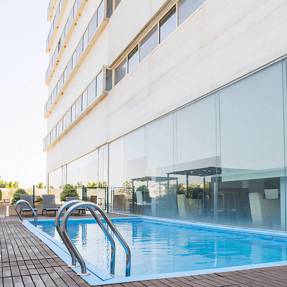 Piscina moderna junto a un edificio con ventanales y terraza de madera.