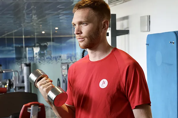 Hombre levantando una pesa en un gimnasio con camiseta roja.
