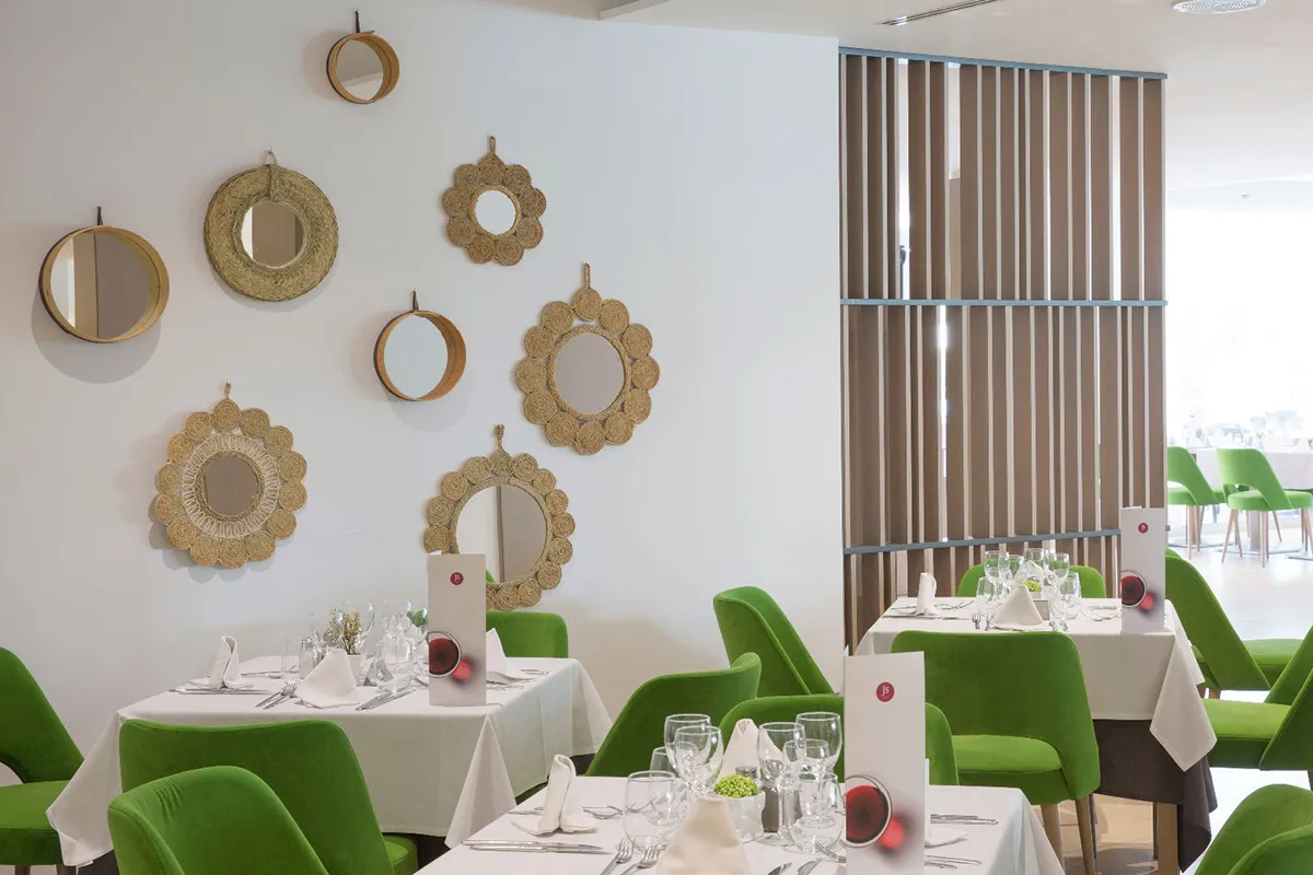 Restaurante con sillas verdes y espejos decorativos en la pared.