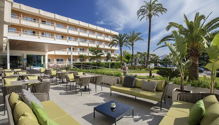 Terraza de hotel con muebles verdes y palmeras rodeada de vegetaci&oacute;n.