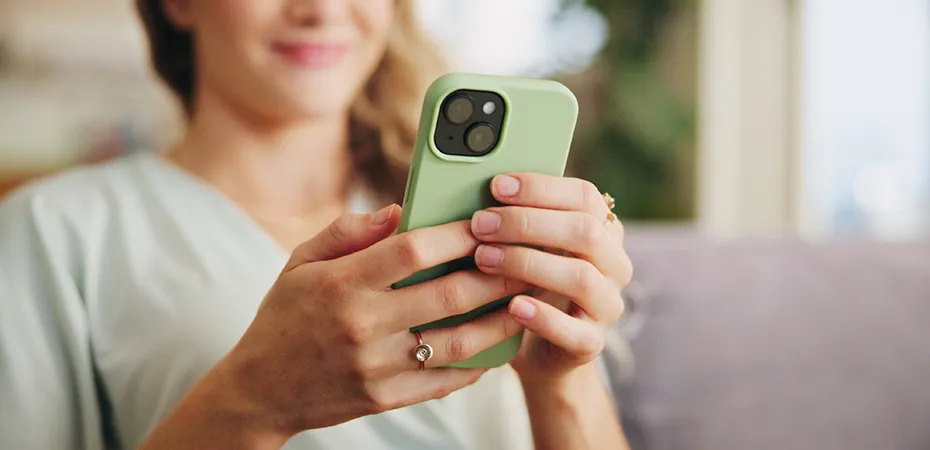 Persona sosteniendo un tel&eacute;fono verde, sonriente, en un entorno acogedor.