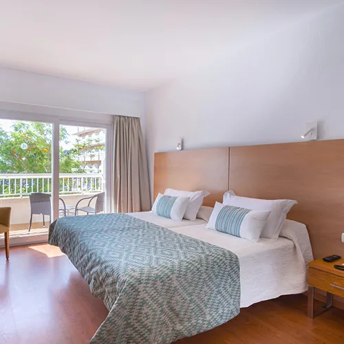 Habitaci&oacute;n luminosa con cama doble, balc&oacute;n y sillas en el exterior.