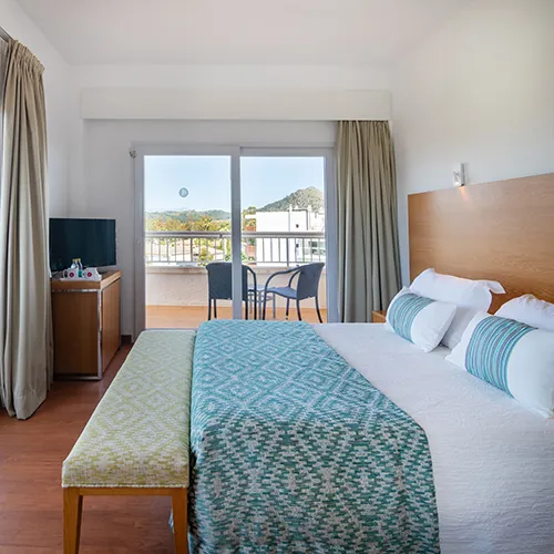 Habitaci&oacute;n de hotel con cama grande, balc&oacute;n y vistas al exterior.