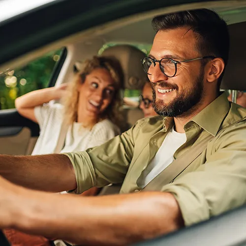 Personas sonrientes dentro de un coche, con el conductor al volante.