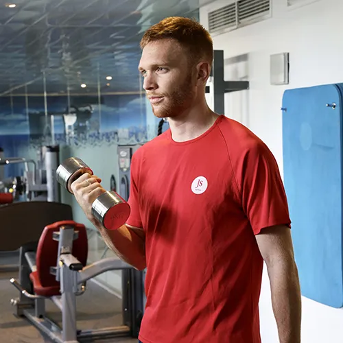 Personaje en gimnasio levantando una mancuerna, lleva camisa roja.