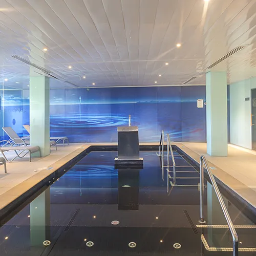 Piscina interior con techo blanco y sillas reclinables alrededor.