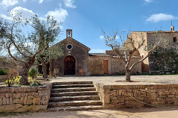 Capilla antigua con &aacute;rboles y escalinata de piedra bajo un cielo azul.