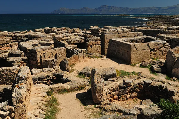 Ruinas antiguas de piedra cerca del mar, con monta&ntilde;as al fondo.