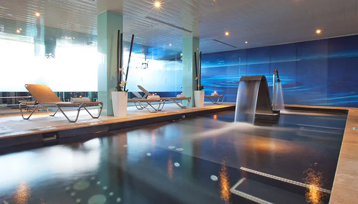 Piscina interior con tumbonas y cascada de agua en un ambiente moderno.