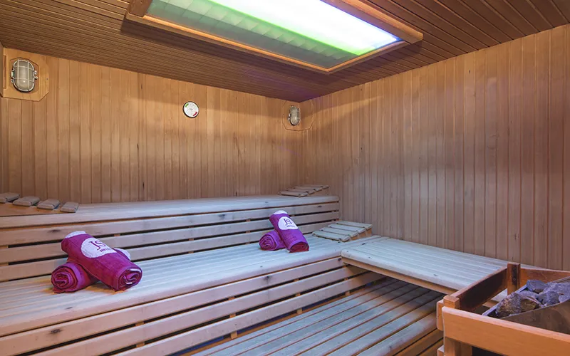 Sauna de madera con toallas rojas dobladas sobre los bancos de varios niveles.