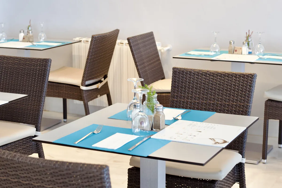 Mesa de restaurante con manteles azules y sillas de mimbre.