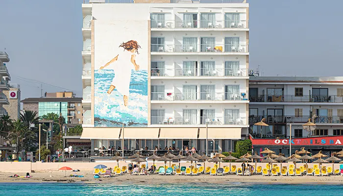 Edificio frente a la playa con mural de ni&ntilde;a sobre el agua.