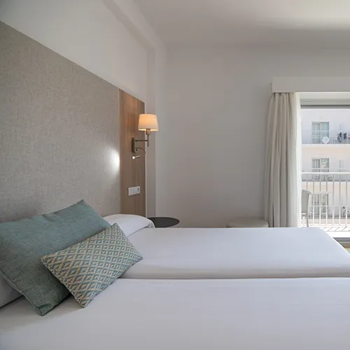 Habitaci&oacute;n de hotel con camas dobles, cojines y l&aacute;mpara de pared.