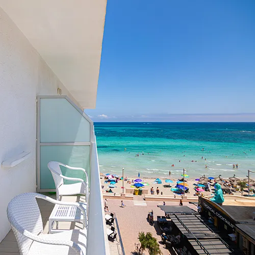 Balc&oacute;n con vista al mar, playa con sombrillas y visitantes disfrutando del sol.
