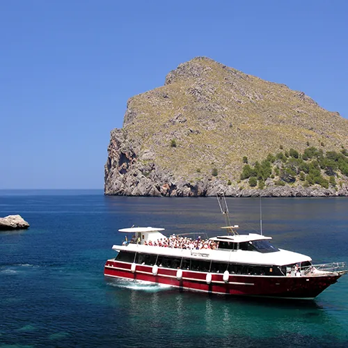 Barco en el mar frente a una gran isla rocosa y cielo despejado.