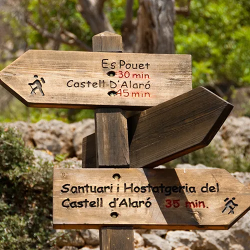 Se&ntilde;al de madera con rutas y tiempos hacia Es Pouet y Castell d'Alar&oacute;.