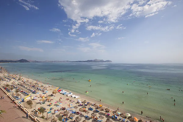 Playa concurrida con sombrillas y ba&ntilde;istas en el mar bajo un cielo despejado.