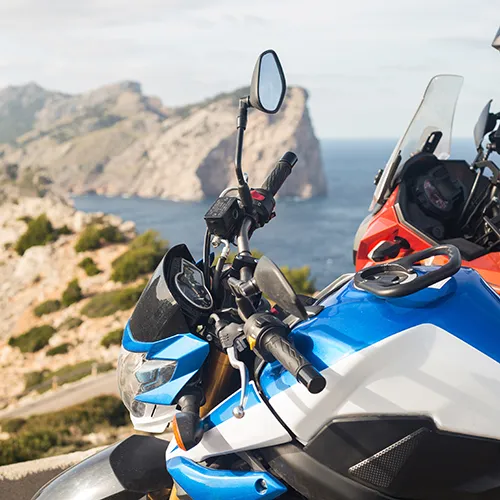 Motocicleta azul y roja frente a un paisaje costero rocoso y el mar.