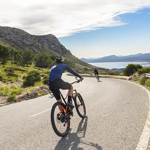 Ciclistas pedaleando en una carretera junto al mar y monta&ntilde;as.